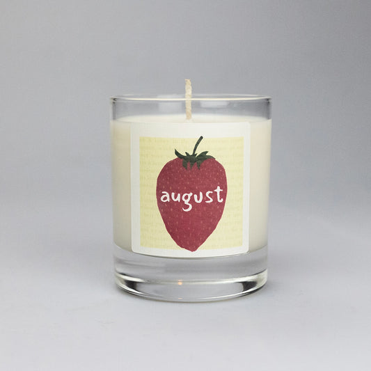 Product photo of scented soy candle August, made by BONKI.  Candle in glass jar. Yellow label with strawberry and writing "August".