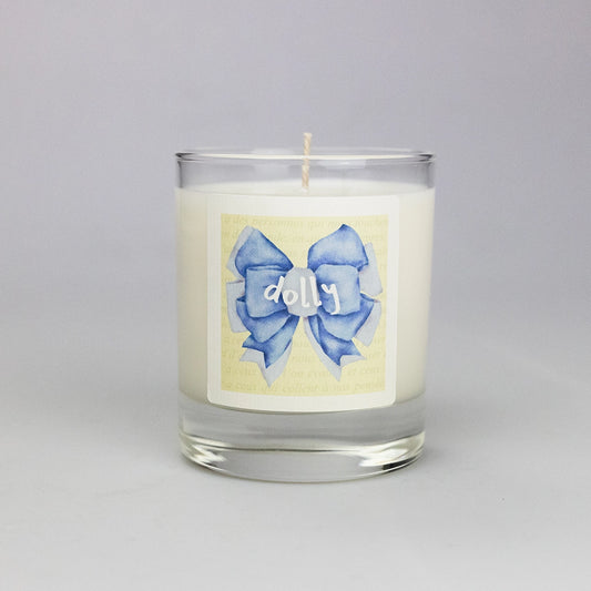 Product photo of scented soy candle Dolly, made by BONKI. Candle in glass jar. Yellow label with blue ribbon and writing "Dolly".